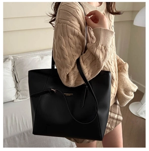 Black leather tote bag shown on shoulder with minimalist fashion details and gold buckle