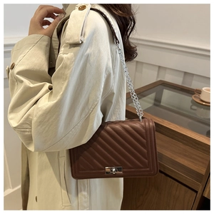Detail of a brown quilted leather crossbody bag with silver chain strap and metal lock