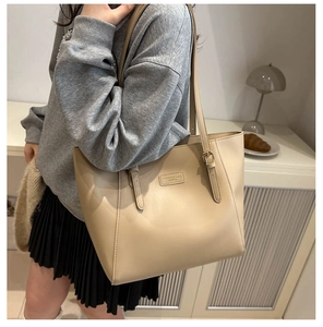 Close-up of beige tote bag featuring rectangular leather patch and adjustable metal buckle