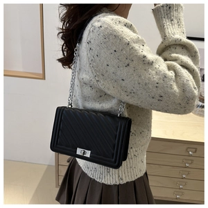 Side view of black quilted crossbody bag with silver chain strap on model's shoulder