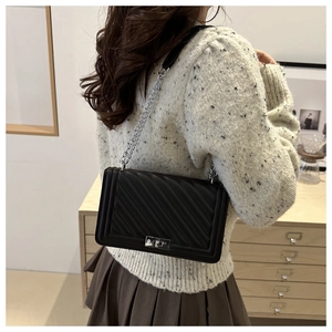 Detail showing the silver metal chain strap and quilted leather texture on a black bag