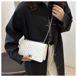 Detailed shot of white quilted chain bag with silver twist lock on black coat