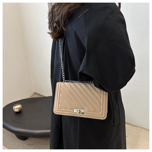 Detail of beige chevron quilted bag with silver lock worn over a black winter coat
