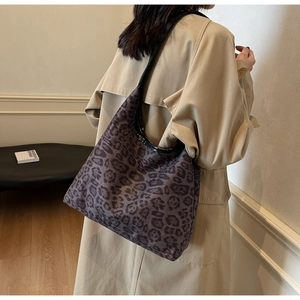 Dettaglio della borsa tote leopardata indossata con trench su uno sfondo dal design sobrio
