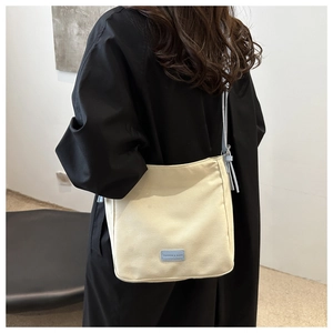 Detail of high-density cream canvas crossbody bag with blue fashion tag and strap