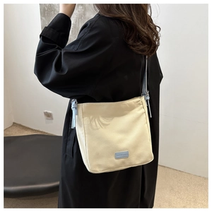 Close-up of beige canvas crossbody bag with blue strap and fashion label on a model