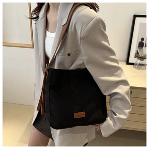 Detail of black canvas tote bag with brown leather patch and adjustable strap worn by model