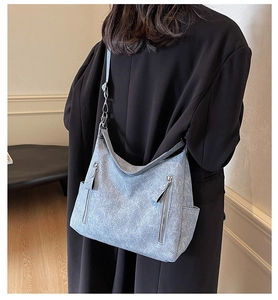 Detail of light blue textured shoulder bag with silver zippers and side pockets on a black coat