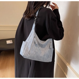 Detail of silver zippers on a light blue faux suede tote bag worn by a model