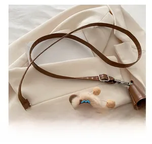Detail of adjustable leather strap and cute plush bear charm on a brown handbag