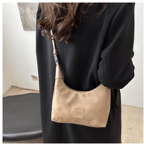 Side view of model wearing a beige suede shoulder bag with a fashion buckle and logo