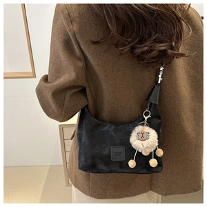 Detail of black matte crescent bag featuring a fashion patch and plush lamb charm