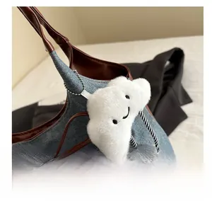 Dettaglio di ciondolo a nuvola in peluche bianco con sorriso su borsa di jeans blu