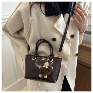 Detail of dark brown leather bucket bag with a cute plush monster charm and gold hardware