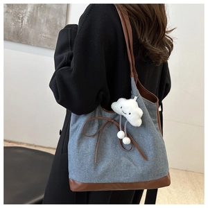 Détail du sac cabas en denim bleu avec lanières en cuir et charme nuage blanc
