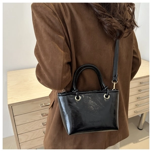 Detail of black glossy handbag with gold hardware and embossed fashion logo text