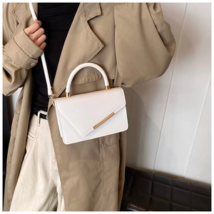 Detail of white litchi pattern leather handbag featuring golden metal trim and asymmetric flap