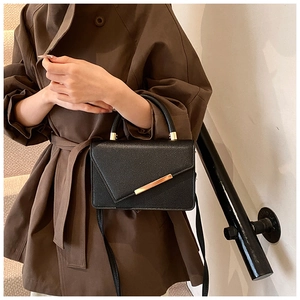 Detail of black pebbled leather crossbody bag with gold hardware and diagonal flap