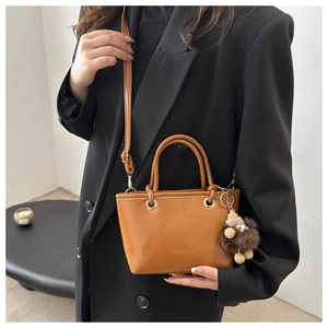 Detail of a brown leather bucket bag featuring a plush charm and fashion typography