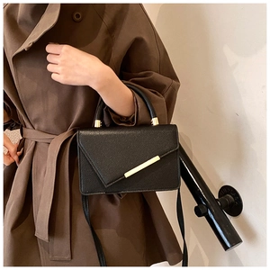 Detail of minimalist black crossbody bag with asymmetric flap and golden metal trim detail