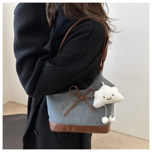 Détail du sac cabas en denim avec base en cuir marron, nœud et breloque nuage en peluche