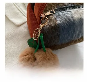 Gros plan sur le charm cerise en peluche avec pompons marrons et feuilles sur sac velours