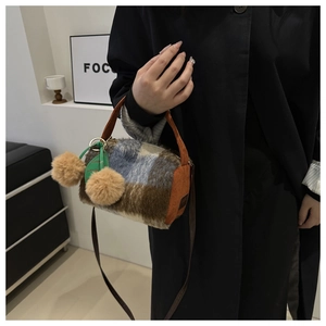 Détail d'un sac polochon en laine à carreaux avec breloques feuille et pompons bruns