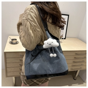 Détail du sac cabas en denim avec finitions en cuir noir, nœud et breloque nuage