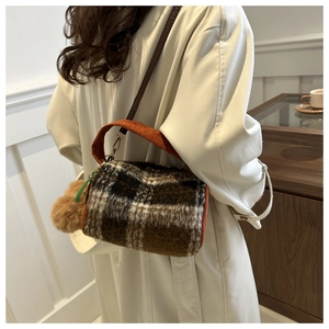 Détail du sac cylindre en peluche à carreaux avec poignée en velours côtelé orange et pompon
