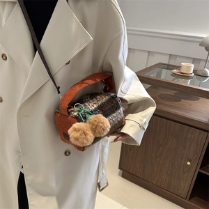 Sac bandoulière en peluche à carreaux marron avec pompons porté sur un manteau blanc