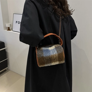 Sac polochon en laine à carreaux avec poignée orange porté sur un manteau noir