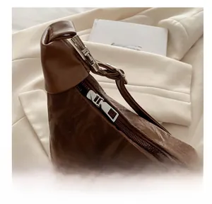 Detail view of the smooth silver zipper and textured brown leather on the shoulder bag