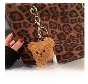 Detail of plush bear charm with woven rope attached to a leopard print tote bag