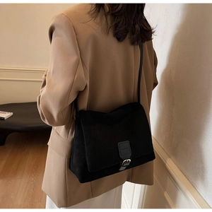 Detail of a black matte suede flap shoulder bag with a metal buckle and slim leather strap