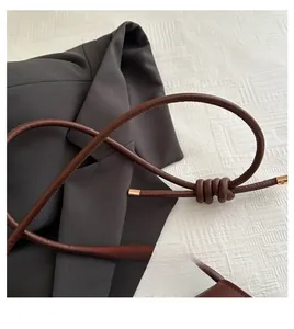 Detail of dark brown leather shoulder bag handle with knot and gold metal tips