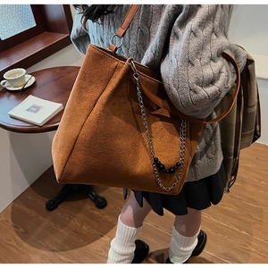 Dettaglio della borsa tote in camoscio marrone con catena in metallo in un caffè autunnale