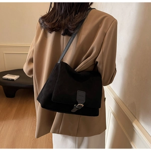 Detail of black suede shoulder bag with leather buckle strap on a model in home setting