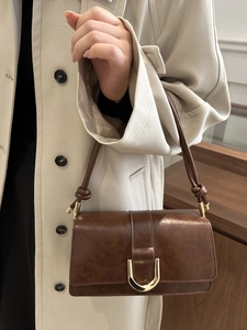 Dunkelbraune Vintage-Leder-Schultertasche mit goldener Schnalle auf beigem Trenchcoat