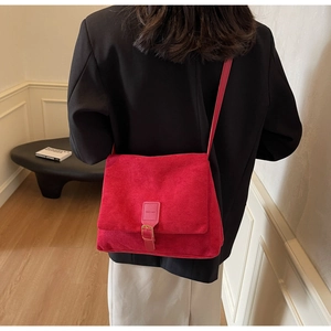 Detail of red suede crossbody bag with gold buckle and smooth matte finish texture