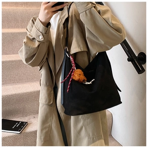 Side view of a large black suede tote bag with a cute teddy bear plush charm on the strap