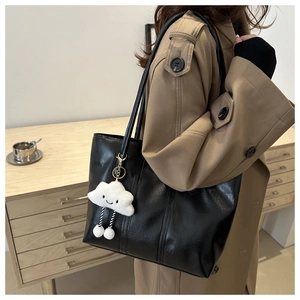 Detail of black faux leather tote bag with cloud charm on a trench coat model