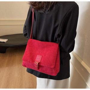 Detailed side view of deep red suede crossbody bag with gold buckle on a model