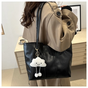 Close-up of black leather tote bag with stylish white plush cloud charm for women