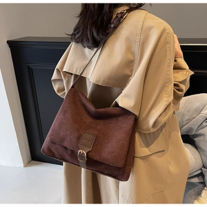 Side view of a vintage dark brown suede messenger bag worn by a model in a trench coat