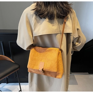 Detail of a ginger suede crossbody bag with pin buckle flap on a beige trench coat
