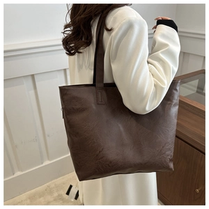 Detalle de bolso tote de cuero marrón oscuro con textura brillante y correas largas