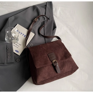 Close-up of vintage brown suede messenger bag with buckle strap on a minimalist setup