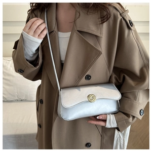 Close-up of a metallic silver shoulder bag with a gold knot clasp and fine chain strap