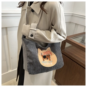 Detail of grey corduroy tote bag with cat embroidery worn by a model in warm light