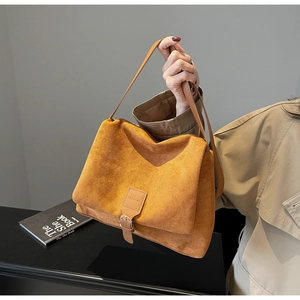 Detailed close-up of mustard yellow suede messenger bag with decorative buckle strap
